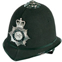 A black British policeman's helmet, the strap peeking out from under, big silver badge on the front